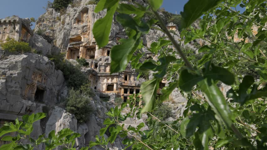 Ancient rock-cut tombs in Myra, Turkey surrounded by lush greenery and dramatic cliffs. Gimbal shot of Myra Ancient City