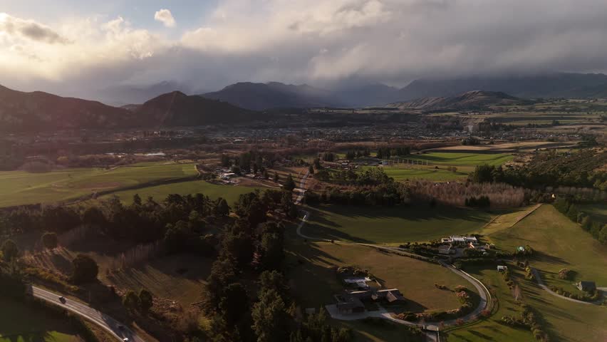 Aerial panoramic view of Wanaka town in New Zealand showing the stunning alpine landscape, waterfront homes under cloudy sky.