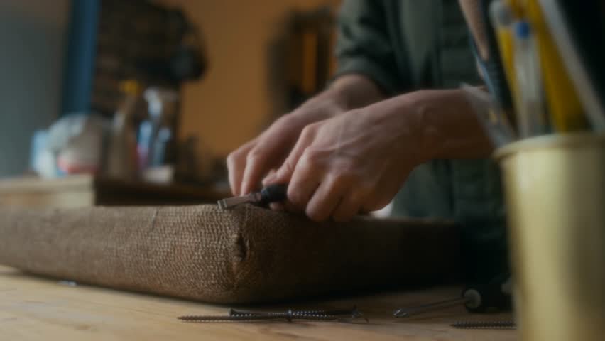 Close-up of a carpenter’s hands removing nails while reupholstering an old chair, highlighting craftsmanship, furniture restoration, and skilled manual work.