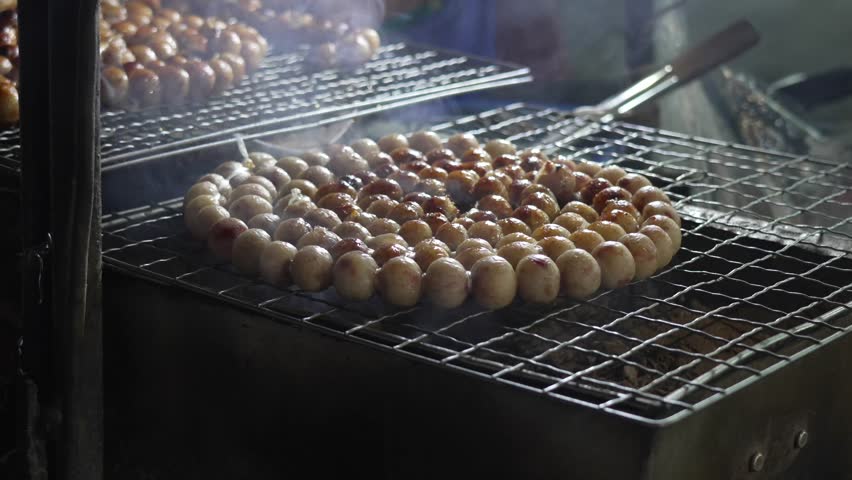 Thai street food vendor grilling delicious Isaan style fermented sausages, 'Sai Krok Isan', on a charcoal BBQ grill, preparing a popular snack at night market in Bangkok, Thailand