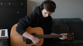 Slow motion close-up of caucasian young musician intently playing chords on acoustic guitar while wearing studio headphones, focusing on technique and creativity of home recording and songwriting. - Powered by Shutterstock - Get 15% off with code: PIKWIZARD15