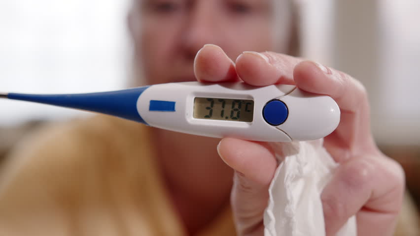 Woman suffering from cold and fever showing digital thermometer with measurement result on display with high body temperature close-up