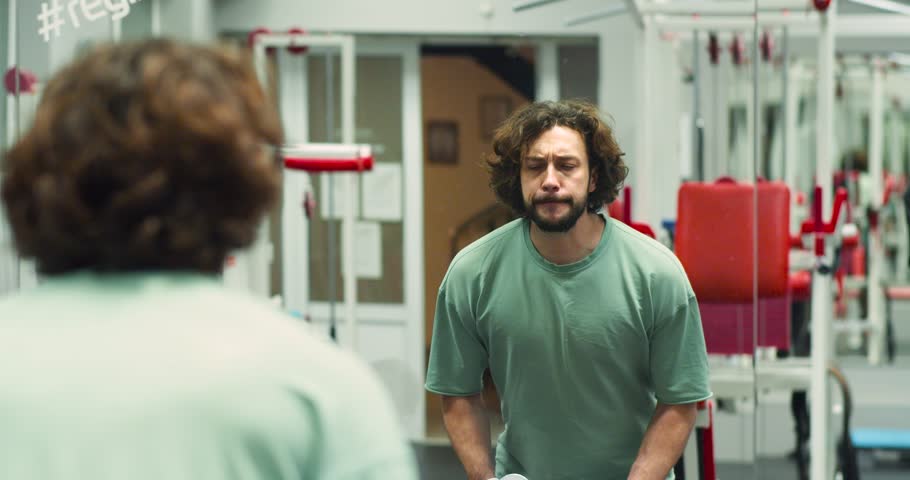 Caucasian man during gym workout in front of a mirror. Standing dumbbell raises for deltoids. Deltoid workout with dumbbells. Slow motion 4k footage.