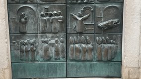 A heavy antique metal door featuring detailed bas-relief carvings and engravings depicting historical scenes. The decorative gate is closed, set within the stone facade of a building in Kotor Old Town - Powered by Shutterstock - Get 15% off with code: PIKWIZARD15