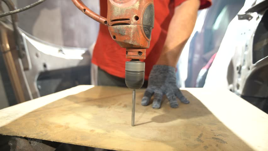 A person is drilling into a piece of wood with care in a workshop. Tools and materials are visible, showing craftsmanship and attention to detail. The atmosphere is productive and creative.