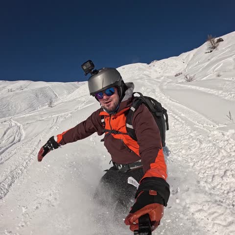 Slow motion 1:1 selfie of a male snowboarder carving through fresh powder off-piste. Square format emphasizing the extreme winter action.