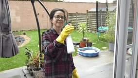 Woman cleaning glass patio doors with spray bottle and yellow gloves in the backyard during the day - Powered by Shutterstock - Get 15% off with code: PIKWIZARD15
