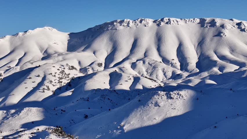 A stunning snowy mountain scene captured by drone, featuring a gondola line, pine-covered slopes, and warm sunrise light. Perfect for themes of winter travel, skiing, alpine landscapes, and nature.