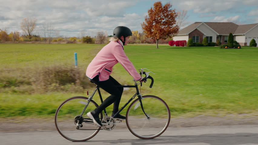 Middle-aged woman riding a bicycle through a quiet American suburban neighborhood, enjoying outdoor exercise and a healthy active lifestyle. High quality 4k footage