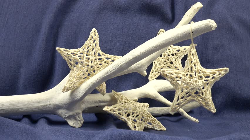 Handmade Christmas decorations white knitted star sway on a decorative white  tree branch against a blue backdrop 