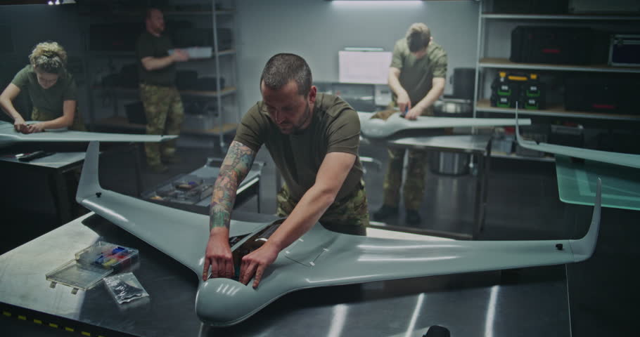 Woman and Men Assembling Advanced Military Drones in Factory. Woman Engineer Works Alongside Male Colleagues, Assembling Advanced Military Drones in Modern Factory Setting. Defense Manufacturing.