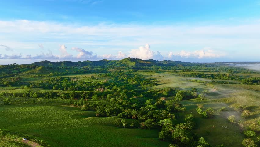 Panoramic mountain range under the clouds. Grassy fields and hills in the evening light. Rural landscape. Summer in the Dominican Highlands. Beautiful summer mountain landscape.