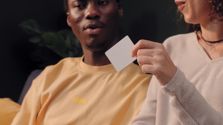 Happy diverse couple making an online payment with a credit card and laptop while sitting on a sofa