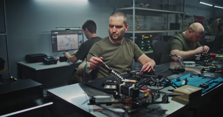 Busy, Well Lit Tech Workshop Shows Multiple Engineers Immersed in Drone Development. Concept of Collaboration, Innovation, and Intense Focus Required For Cutting Edge Electronics Production.