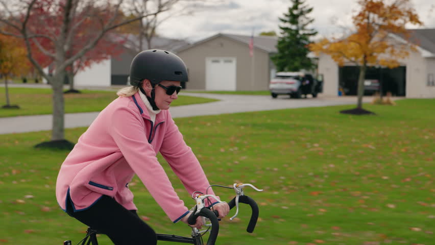 Middle-aged woman cycling through a suburban American neighborhood in autumn, promoting healthy living and outdoor activity. High quality 4k footage