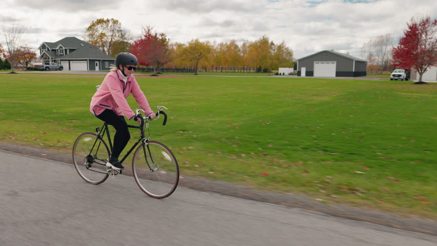 Middle-aged woman cycling past suburban American houses in autumn, enjoying an active and healthy outdoor lifestyle. High quality 4k footage