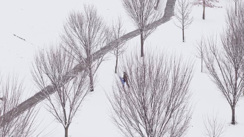One person playing in the snow and hiking up hill holding a snowboard to play in snow-covered environment in Columbus, Ohio weather and winter season on day off cause snowstorm from drone shot aerial