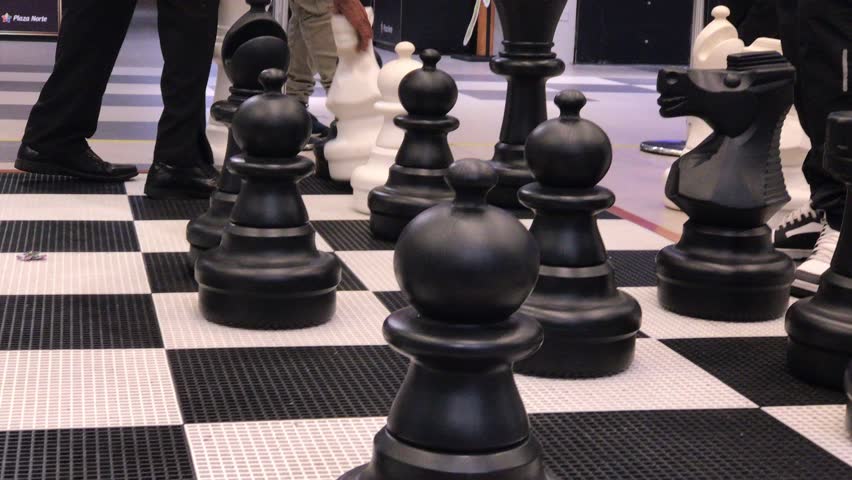Large black and white chess pieces arranged on a giant chessboard for a game in a public space