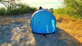 Cinematic video showing a woman emerging from a blue camping tent under warm morning sunlight with the Black Sea visible in the background. - Powered by Shutterstock - Get 15% off with code: PIKWIZARD15
