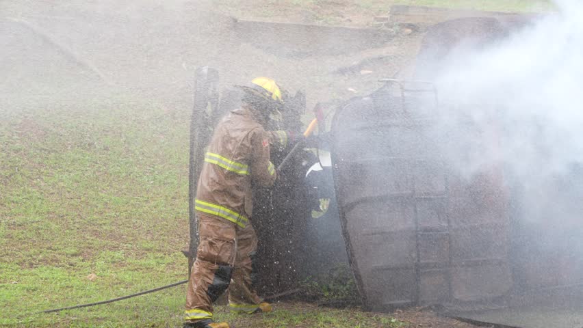 Firefighters practicing fire extinguishing, running out to see smoke and flames on an old car.