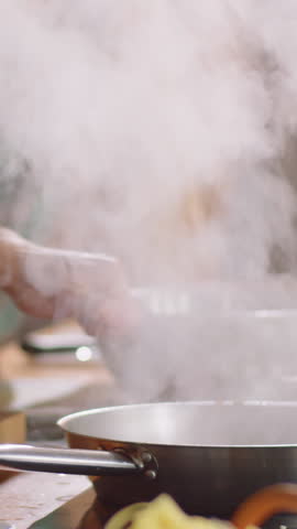 Vertical close-up shot of unrecognizable chef flambeing dish in pan while excited students looking during master class
