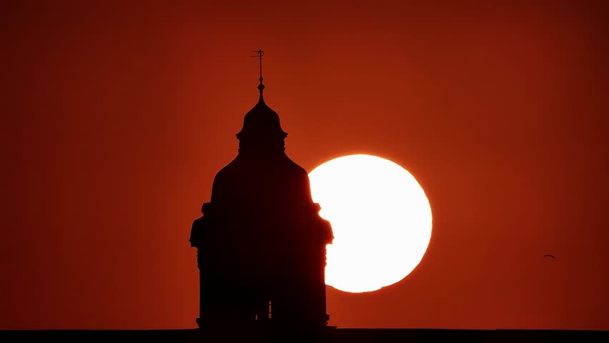 Handheld zoom video shows the Varna Railway Station tower silhouetted against a large setting sun, creating a warm orange background, Varna, Bulgaria, 20 Aug, 2019