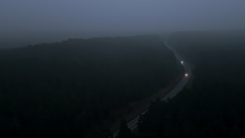 Dark winding highway illuminated lights, Illuminated distant village lights along winding foggy highway