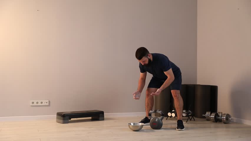 Man clapping hands with talcum powder before training with kettlebell in gym