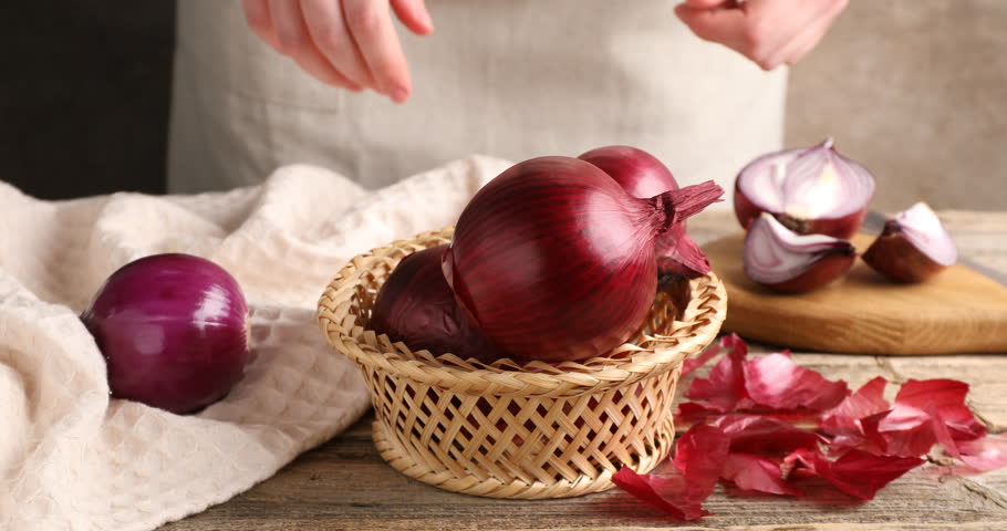 Woman peeling fresh onion bulb at wooden table, closeup