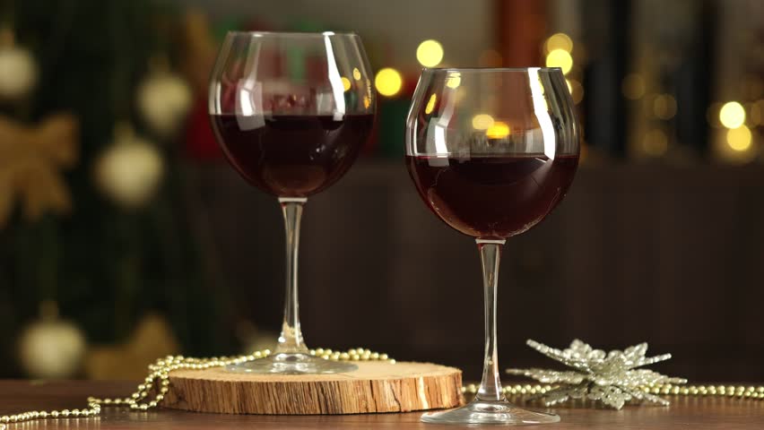 Women clinking glasses of red wine at wooden table against blurred lights, closeup. Christmas and New Year celebration