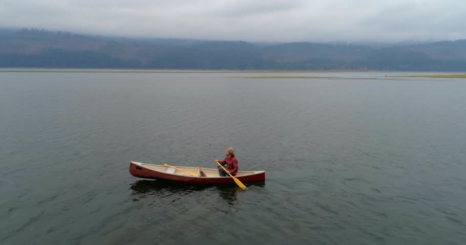 Man starting strokes, paddling canoe for leisure on lake, drone tracking, tech HUD over paddler. Watercraft, solitude, aerial, overcast, outdoors, wake, overlay