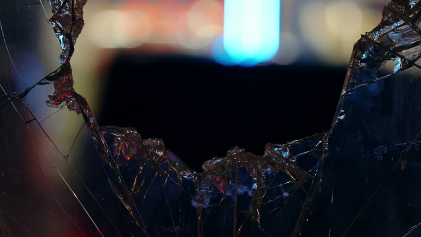 Close-up of a shattered glass window with a jagged circular hole revealing blurred city lights and a vertical neon glow, highlighting sharp edges against a defocused urban backdrop