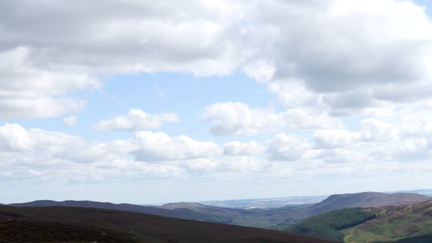 Wide panning shot of Scottish Highlands valley, heather moorland, cloudy sky, natural daylight