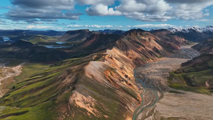Aerial view of Landmannalaugar’s colorful volcanic ridges and winding river valley, showcasing Iceland’s dramatic highland scenery in bright summer light.
