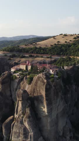 Vertical slow aerial shot of Saint Stephen Monastery (Agios Stefanos) perched atop a cliff in Meteora, Greece, with parallax motion.