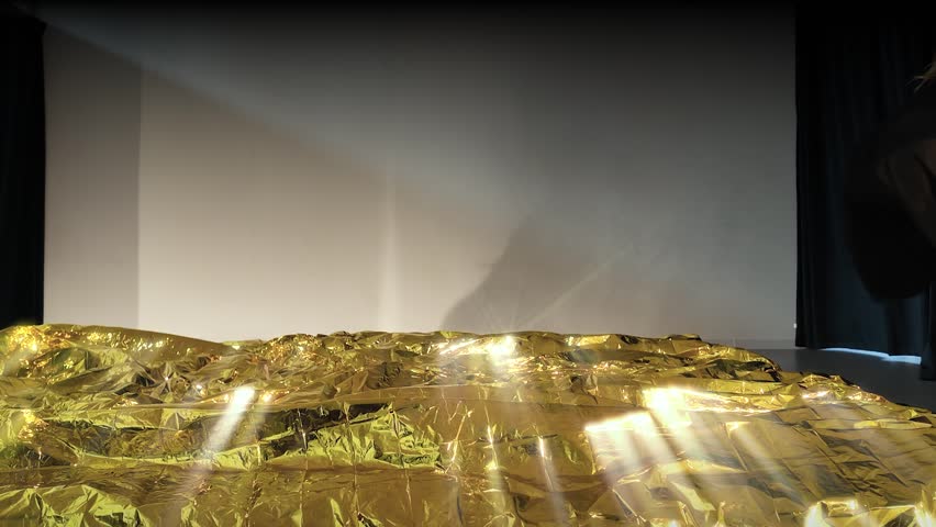 Dancer falling backwards on a mat covered with a gold thermal blanket