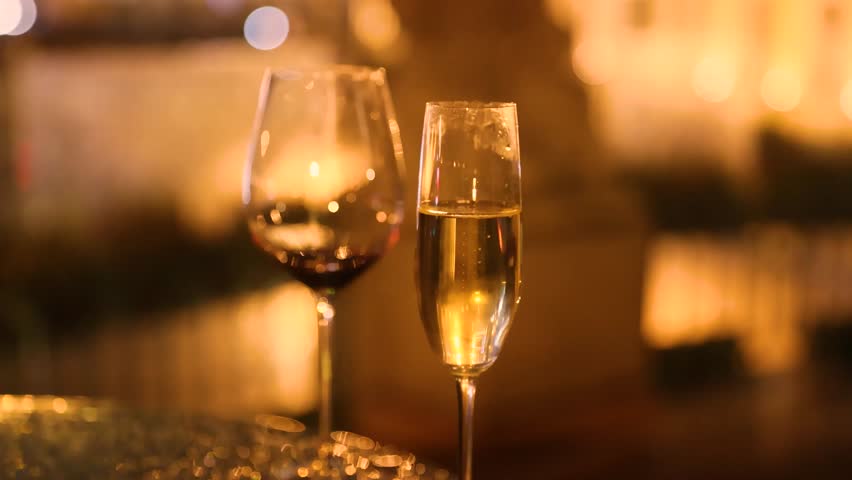 Closeup of two glasses one for champagne and one for wine with sparkling reflections warm evening light and cozy cinematic lamp atmosphere capturing half full drinks and romantic mood