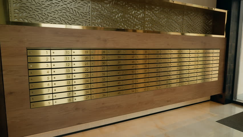 Expansive wall of numbered brass mailboxes integrated into a wood-paneled lobby, highlighting polished metal plates, rivets, and refined contemporary interior design