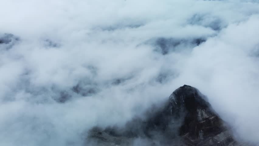 Drone shot of steep mining paths winding through rocky terrain, wrapped in thick mountain fog for a mysterious industrial atmosphere. Ideal for geology studies, risk assessment, and environmental