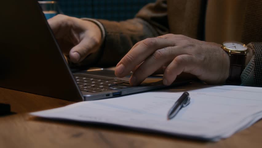 Close-up of hands of an anonymous male journalist or podcast host typing on a laptop and taking notes.