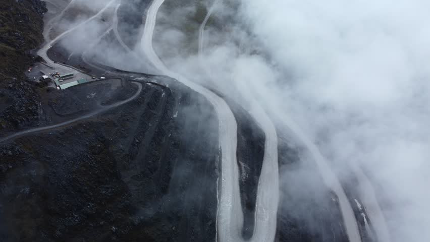 Aerial view of winding mining road covered in dense mountain fog, creating a dramatic landscape for industry, geology, and environmental projects. Perfect for editorial, infrastructure,