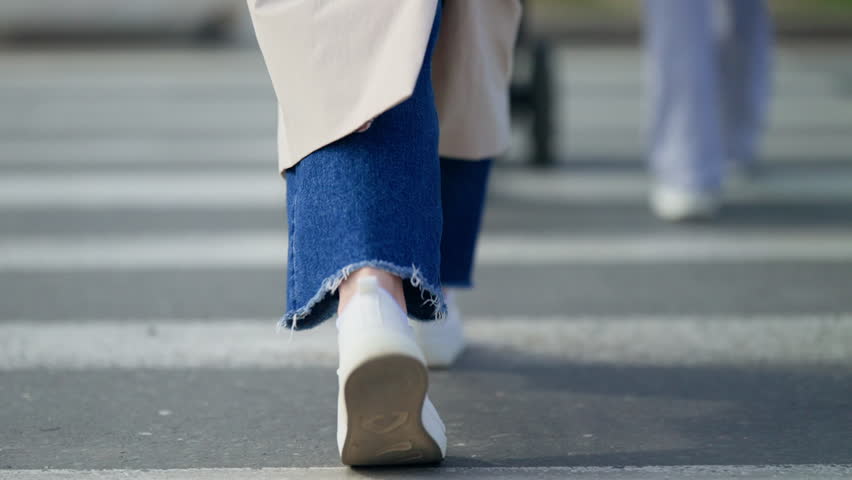 Close-up of casual white sneakers and frayed-hem denim stepping across a city crosswalk, capturing the motion of pedestrians walking on an urban street during a daytime commute