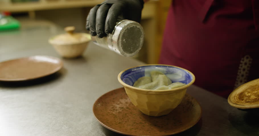 Restaurant service. Culinary process. Chef shaking powdered sugar on sweet dumpling bowl closing lid. Portion hot dish with sour cream sauce.