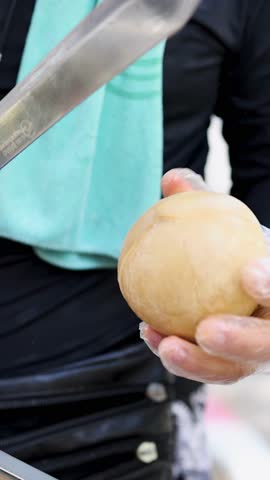 Gloved vendor skillfully slices coconut with machete, bright outdoor lighting, close-up perspective