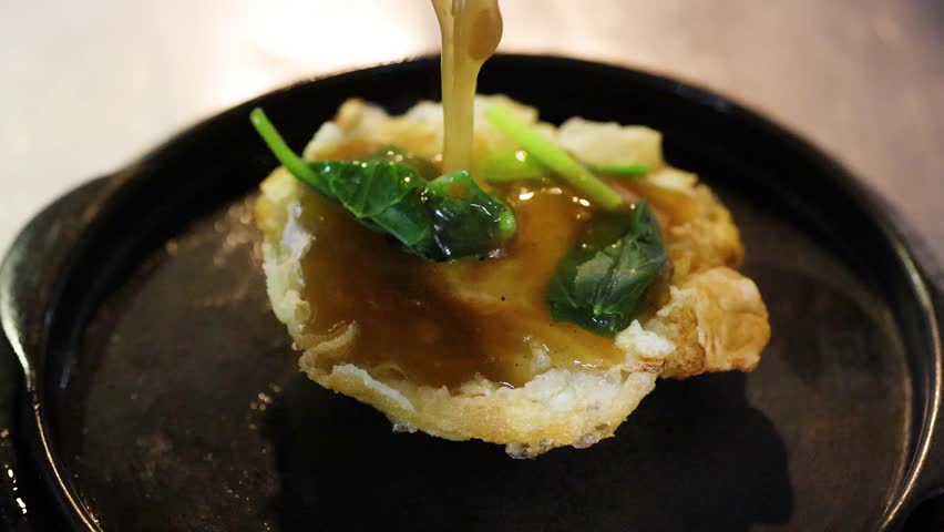 Seafood rad na sauce poured over crispy noodles on sizzling hot plate under night lighting.