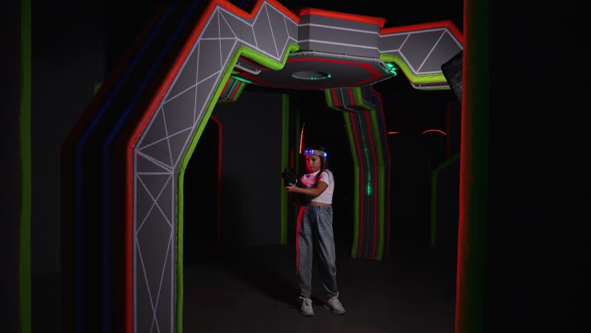 Portrait of a girl with a laser gun having fun in a dark laser tag arena. A girl with a laser weapon in the play area. There are glowing sensors on her head.