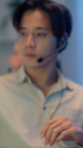A close-up side profile of a male call center agent or IT support representative resting his eyes with his headset around his neck, showing fatigue from working late.
