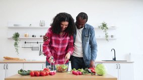 An African American couple is happily preparing a salad together in a bright, modern kitchen, embracing and smiling. - Powered by Shutterstock - Get 15% off with code: PIKWIZARD15