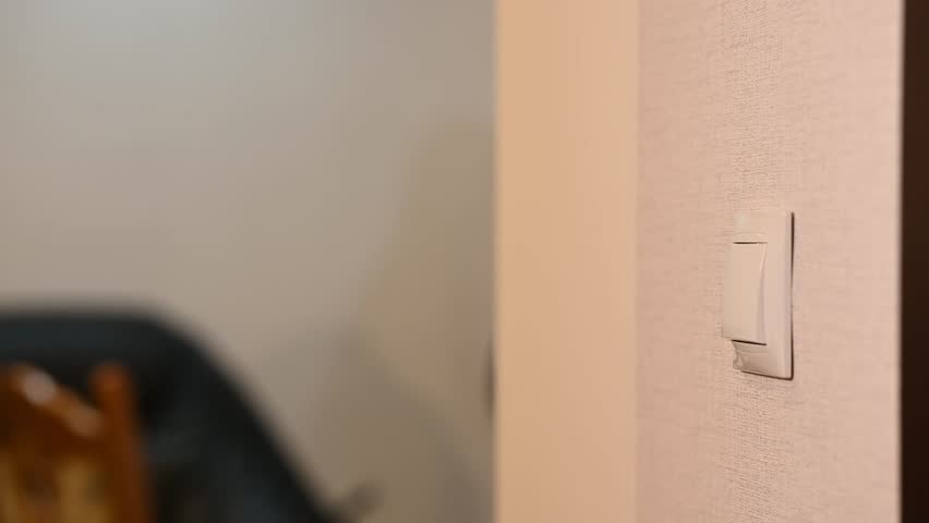 Close-up of a hand switching off a wall light switch indoors, illustrating home electricity control, energy saving, and everyday household actions.
