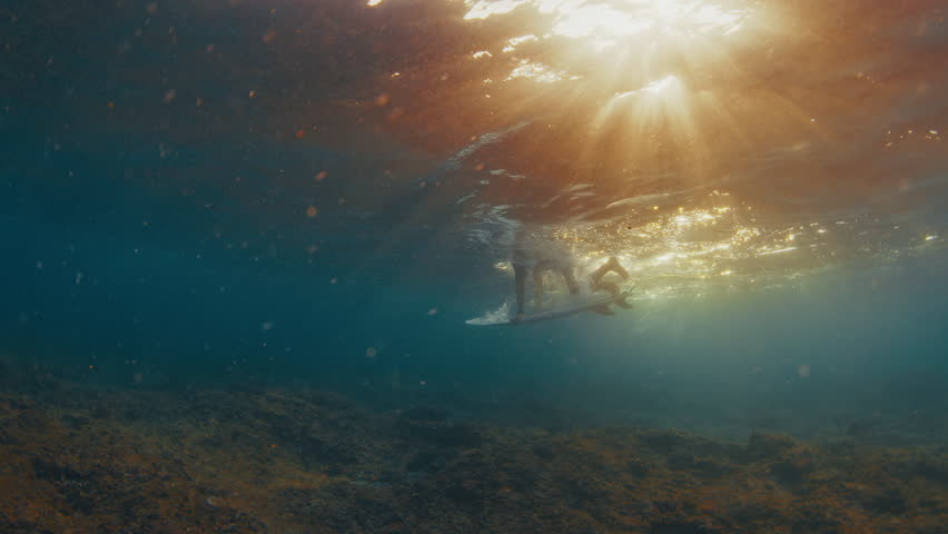 Surfer dives under the ocean wave with surfing board and passes it. Underwater view of the surfer doing duck dive trick